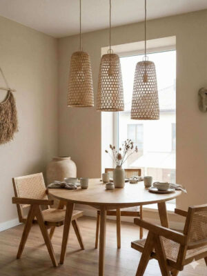 Trzy lampy z bambusa zawieszone nad okrągłym drewnianym stołem w mieszkaniu urządzonym w stylu japandi.
