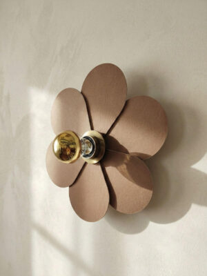 Lampa ścienna kwiatek brązowa mała na tle jasnej ściany. Widok z profilu. Złota żarówka.