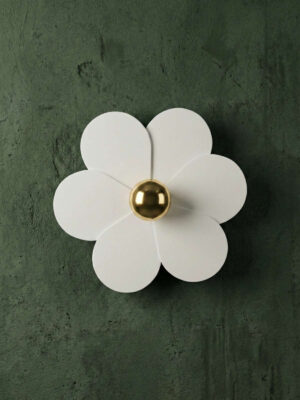 Kinkiet w kształcie białego kwiatka ze złotą żarówką na tle glinianej zielonej ściany.