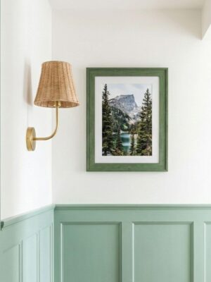 Lampa ścienna z abażurem z rattanu na złotym pałąku w przedpokoju nad angielską boazerią w miętowym kolorze.