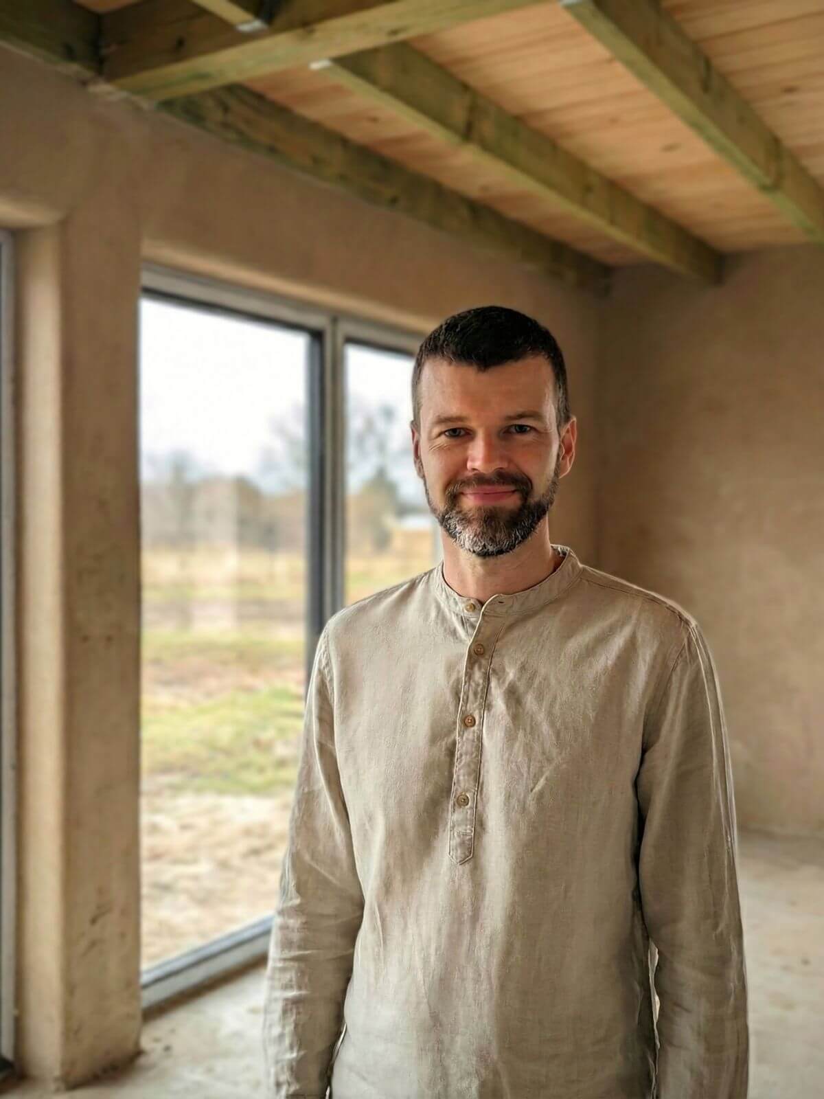 Zdjęcie mężczyzny z brodą w lnianej koszuli w surowym pomieszczeniu w trakcie budowy.