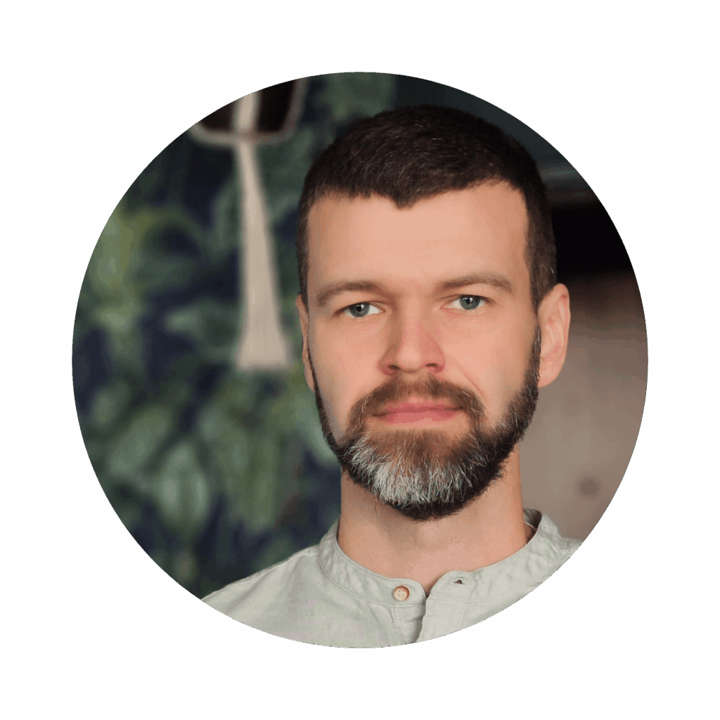 Młody mężczyzna z brodą na tle ściany z tapetą w rośliny.