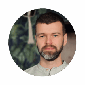 Młody mężczyzna z brodą na tle ściany z tapetą w rośliny.