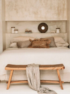 Drewniane ławka przed łóżkiem w surowej sypialni urządzonej w balijskim stylu.