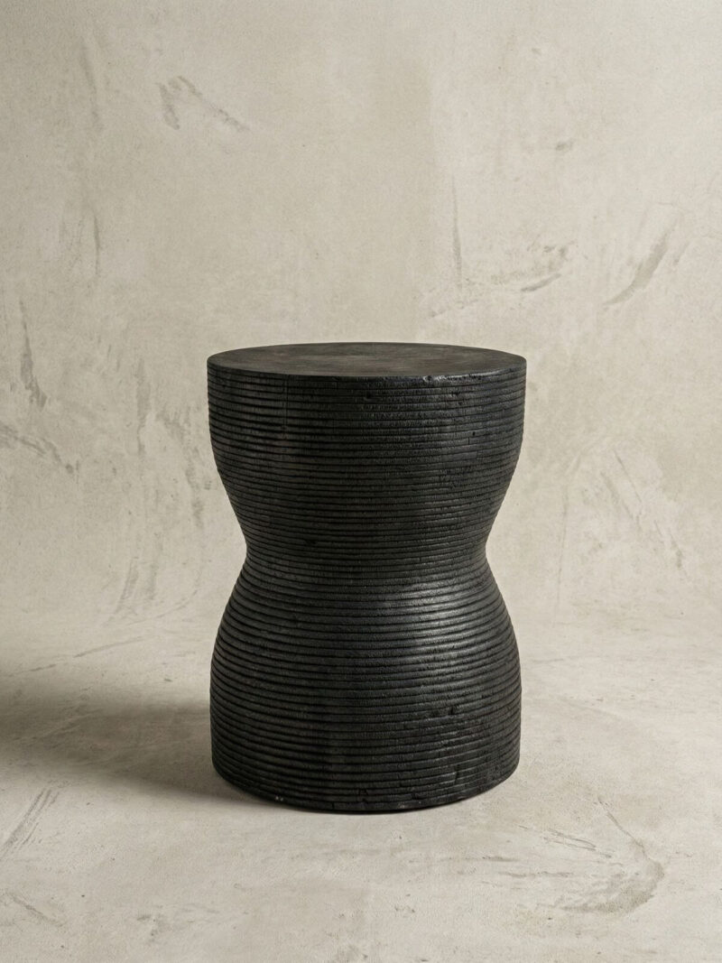 Stołek drewniany japandi Kotoran na tle surowej jasno-szarej ściany.